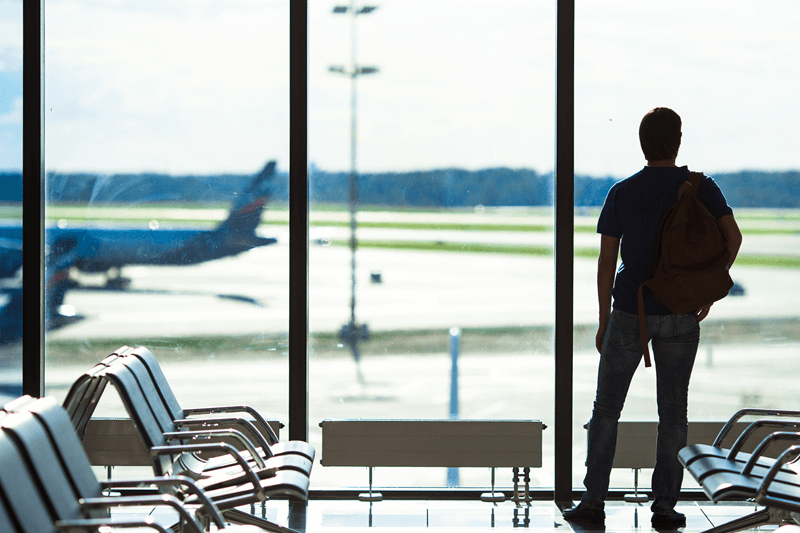 Pessoa em aeroporto observando avião pela janela, representando o início de uma experiência de intercâmbio educacional no exterior