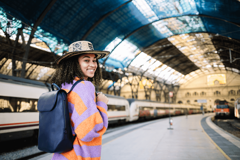 Estudante sorridente com mochila em estação de trem, simbolizando mobilidade internacional e aprendizado cultural durante o intercâmbio