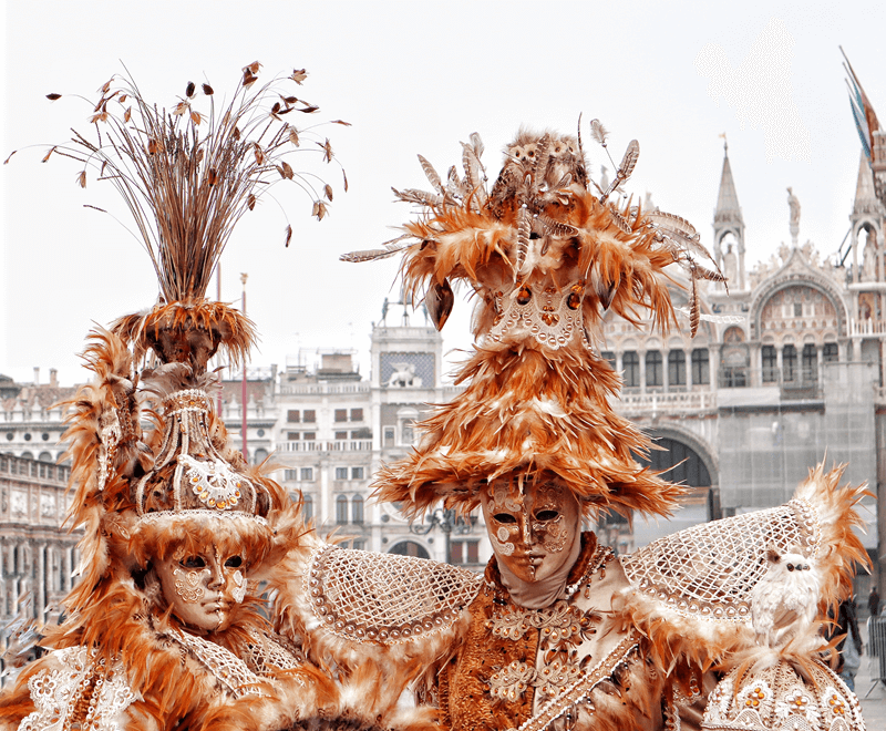 Pessoas com máscaras e fantasias luxuosas do Carnaval de Veneza na Praça de São Marcos, na Itália, com trajes dourados e adornos de penas.
